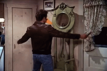 a man in a leather jacket is standing in front of a green coat rack with a mirror on it .